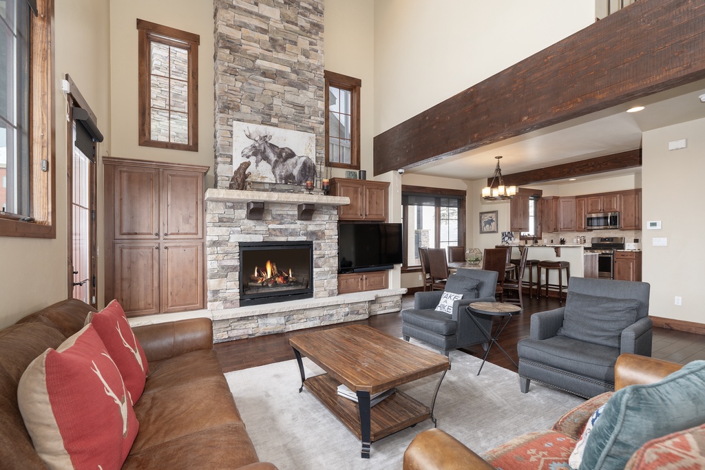 Gather around the crackling stone fireplace in this stunning open-concept space, where rustic beams and warm wood blend seamlessly with your mountain getaway comfort.