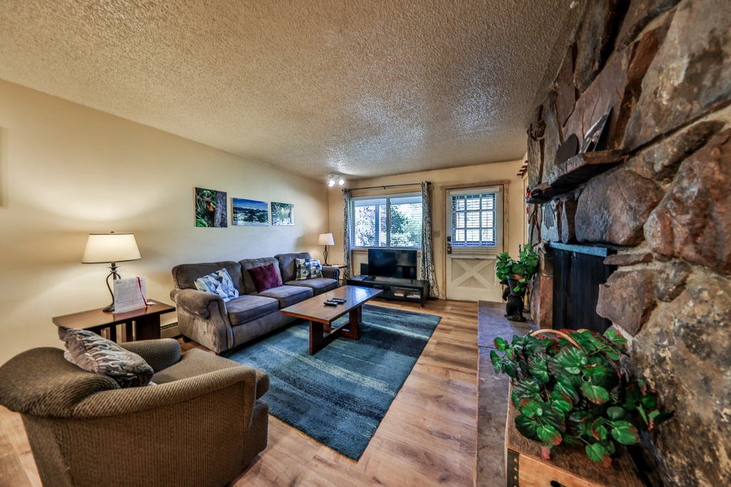 Unwind in your cozy living room with plush seating, warm stone fireplace, and natural light streaming through large windows.