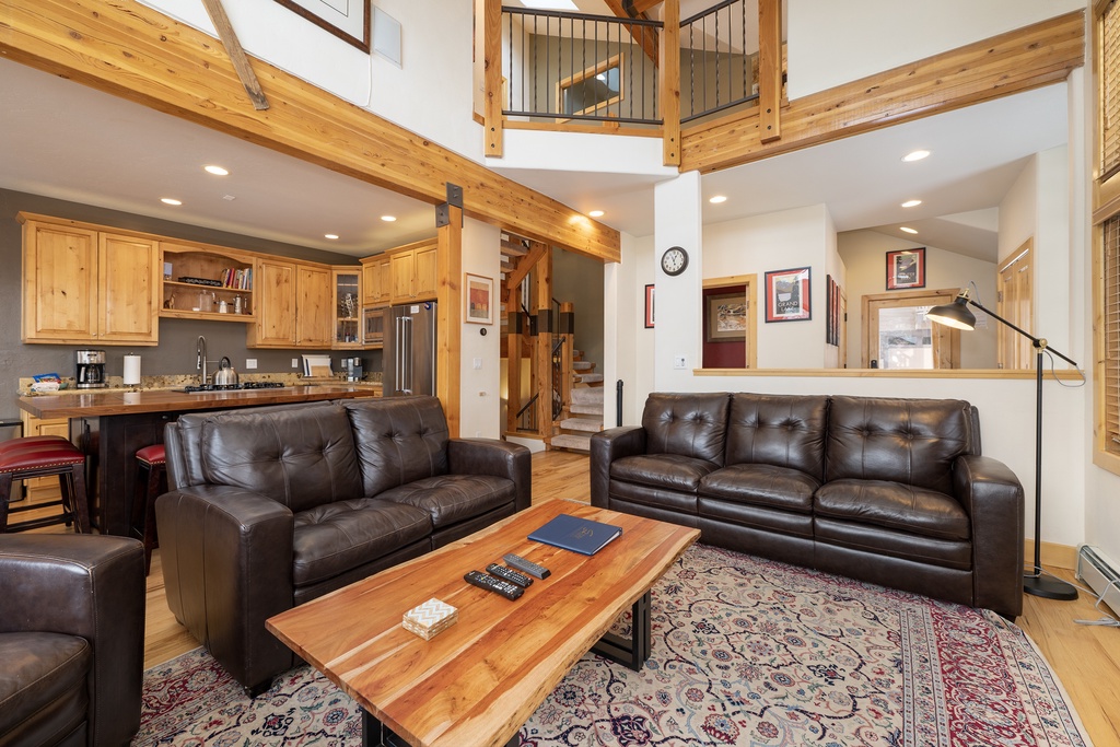 Relax in your spacious open-concept living area with rich leather seating, warm wood accents, and soaring ceilings that create an inviting mountain retreat atmosphere.