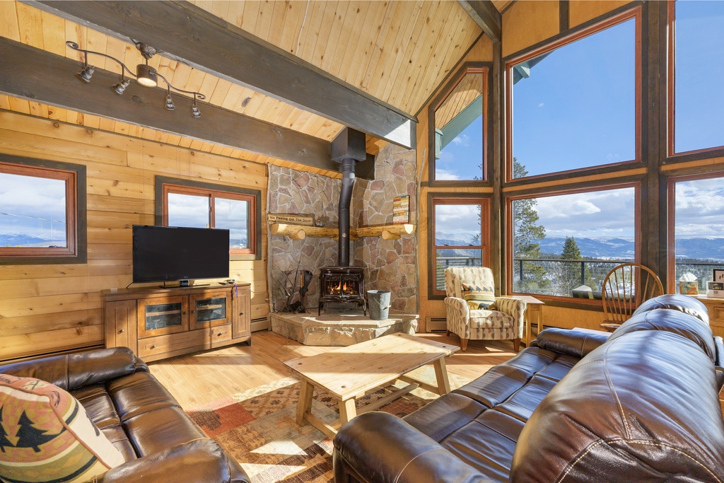 Cozy up in this stunning mountain cabin living room with leather seating, crackling fireplace, and breathtaking panoramic views through floor-to-ceiling windows.