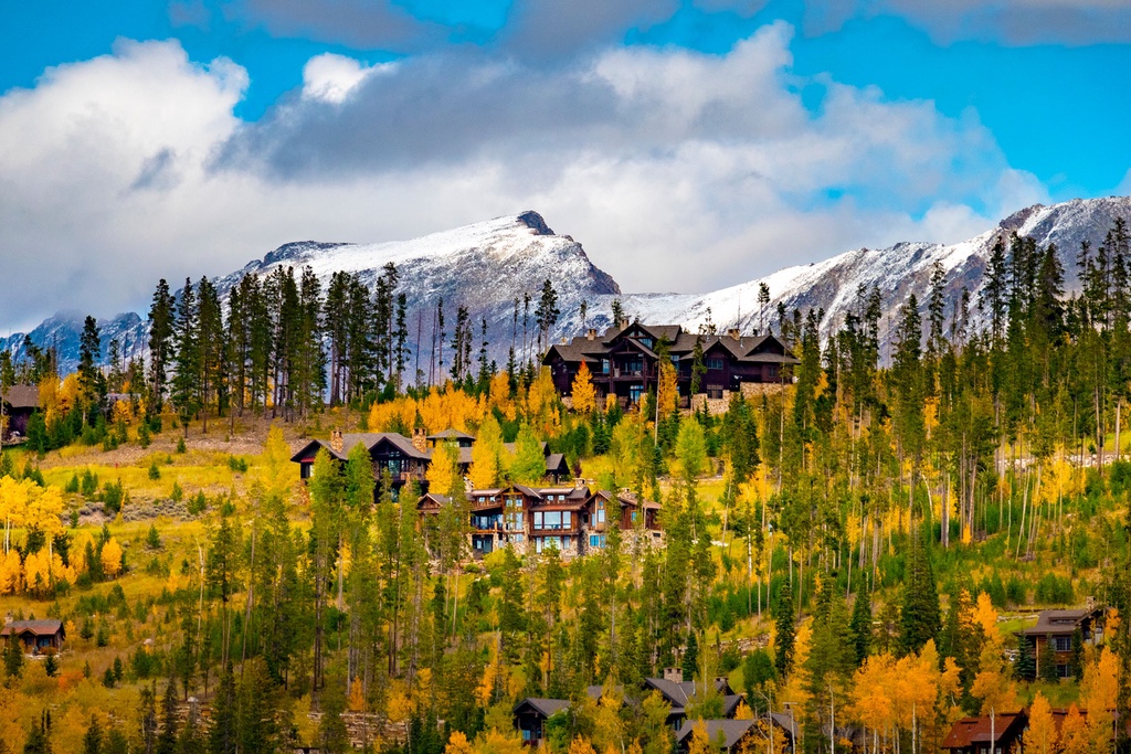 Mountain lodges nestled among golden aspens and evergreens with snow-capped peaks forming a dramatic backdrop.