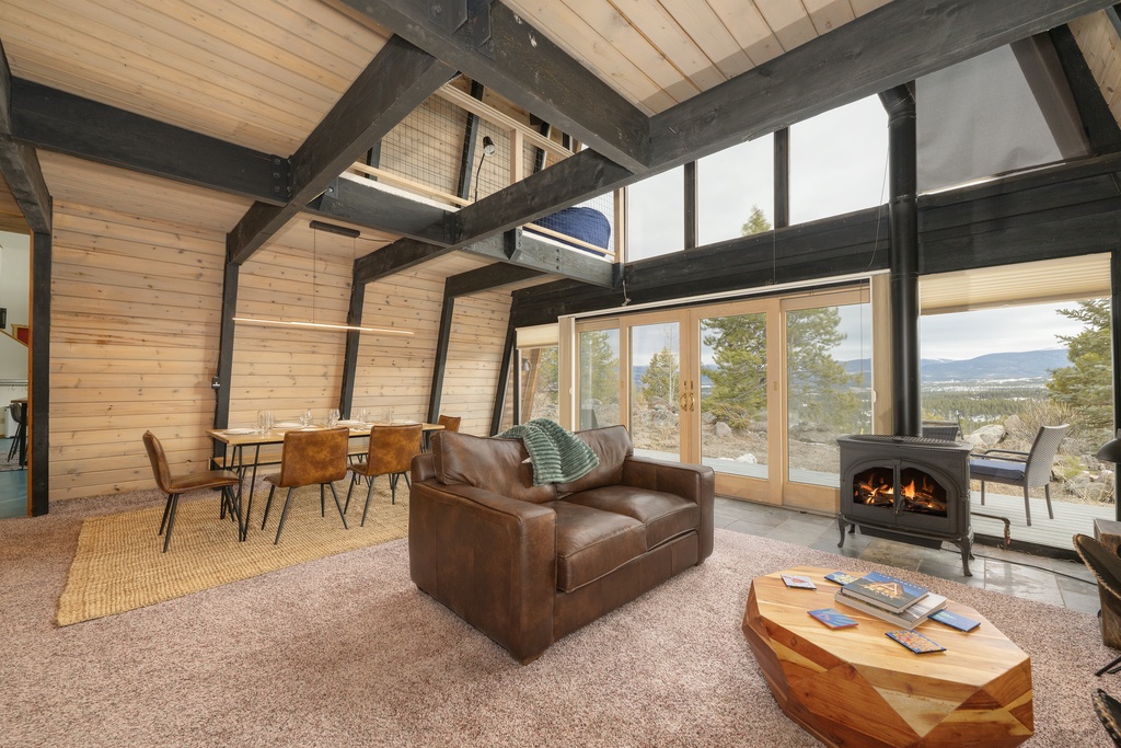 Cozy up in your rustic living room with exposed beams, crackling fireplace, and stunning mountain views through floor-to-ceiling windows.