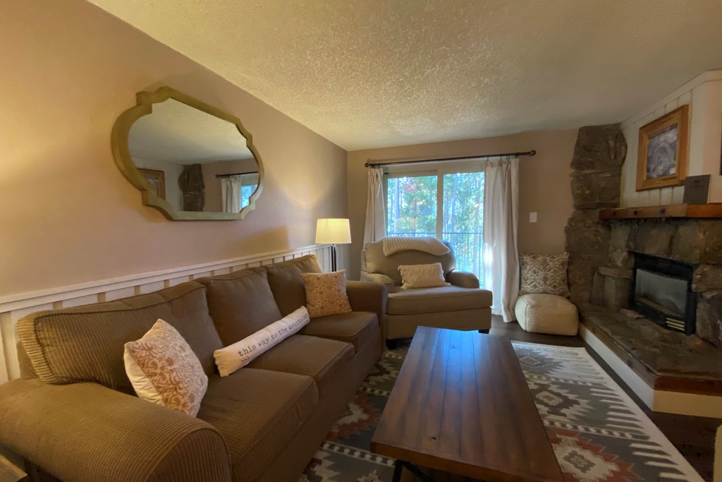 Relax in your cozy living room with plush seating, warm fireplace, and peaceful forest views through sliding doors.
