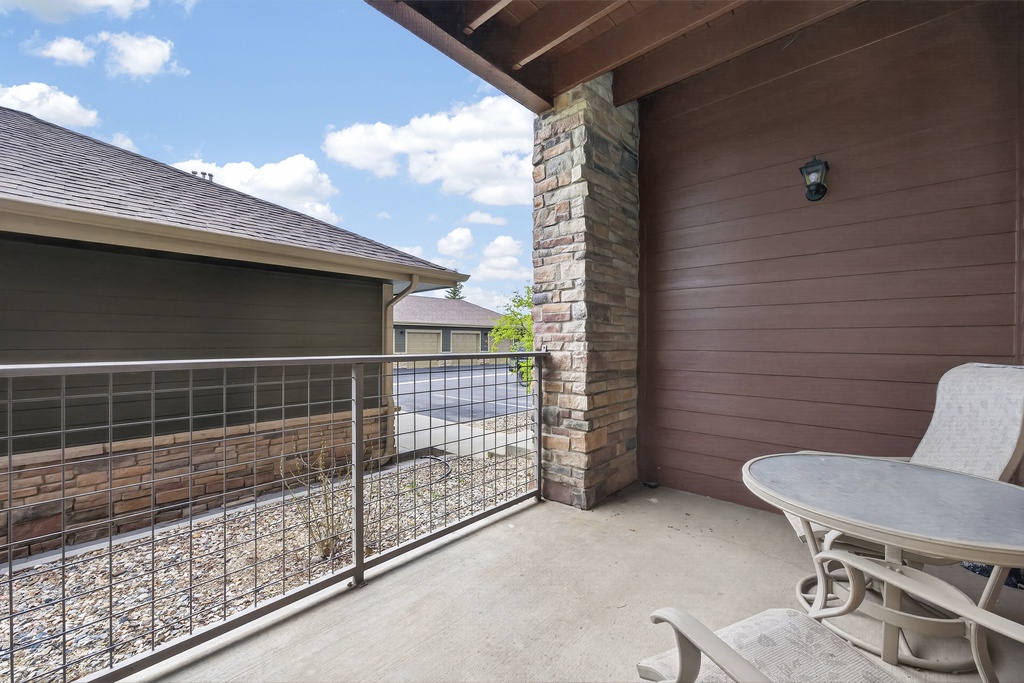 Private covered balcony with seating area overlooking a quiet residential neighborhood. The stone column and wooden ceiling add warmth and charm to this outdoor retreat.