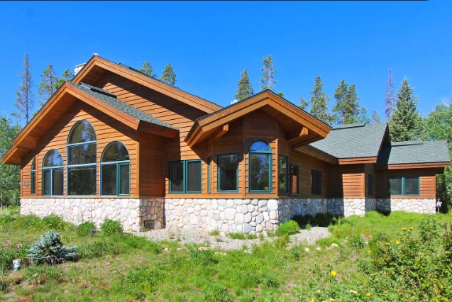 Rustic mountain lodge featuring natural stone and wood construction, nestled among grassy area in a peaceful summer setting.