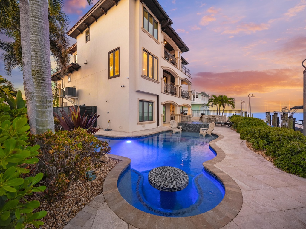 Stunning waterfront villa with elegant pool and breathtaking sunset views over tropical paradise.