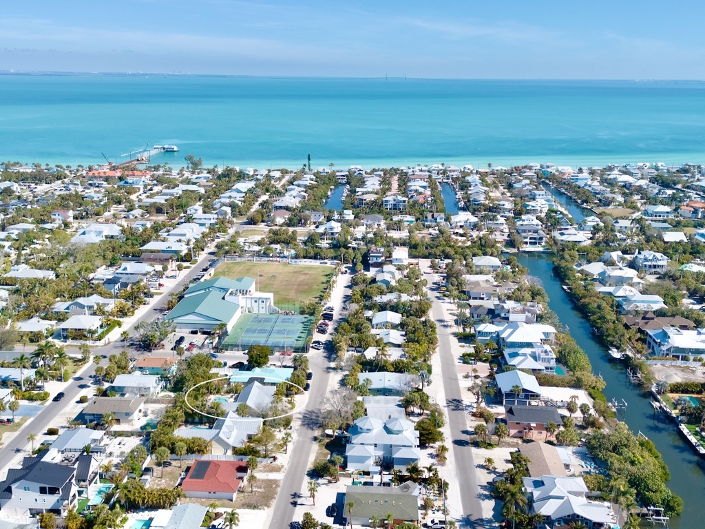 Aerial view of a tropical waterfront community with canal-front homes and pristine turquoise waters stretching to the horizon.