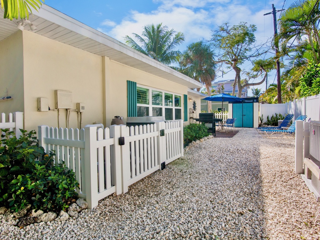 Charming tropical property exterior with white picket fence and palm tree landscaping in a peaceful residential setting.