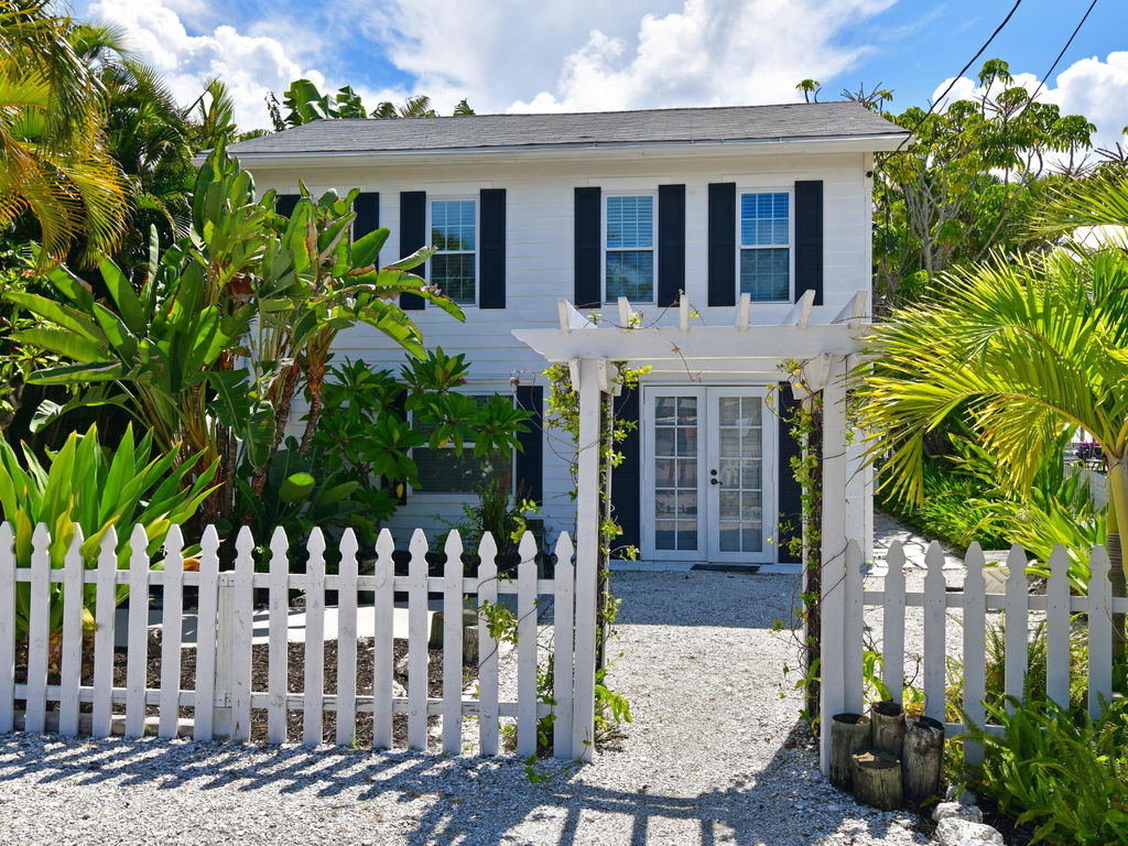 Charming tropical cottage with white picket fence and lush palm gardens creates the perfect island getaway entrance.