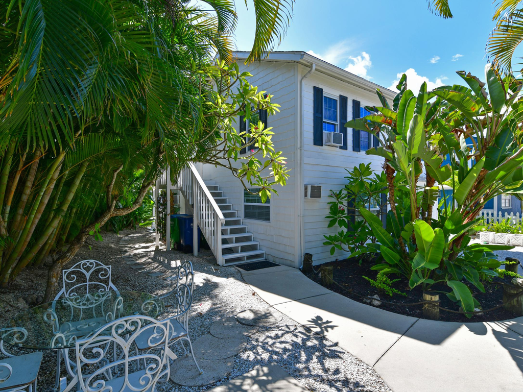 Charming white cottage with blue accents nestled among tropical palms and lush landscaping, perfect for a peaceful getaway.