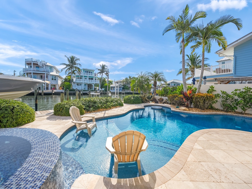 Sparkling pool, spa, and waterfront views framed by swaying palms.