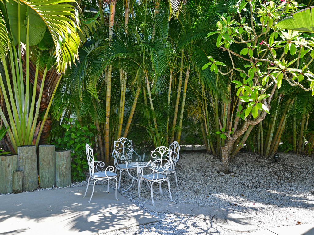 Your private tropical escape awaits with elegant white iron furniture nestled beneath swaying palms and lush bamboo.