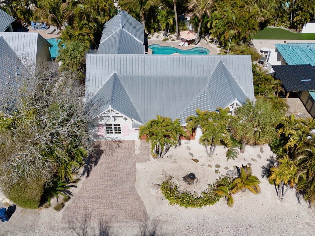 Aerial view of a tropical coastal property featuring charming architecture surrounded by swaying palm trees and neighboring pools in a serene island setting.