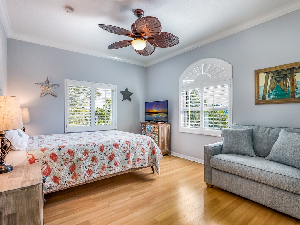 Relax in your bright, airy bedroom with coastal charm, comfortable seating, and tropical ceiling fan keeping you cool.
