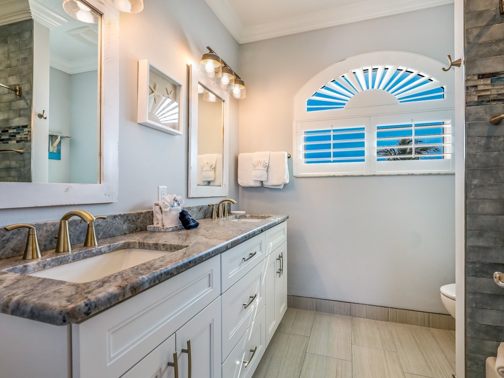 Step into your elegant master bathroom with dual vanities, marble countertops, and ocean views from your arched window.