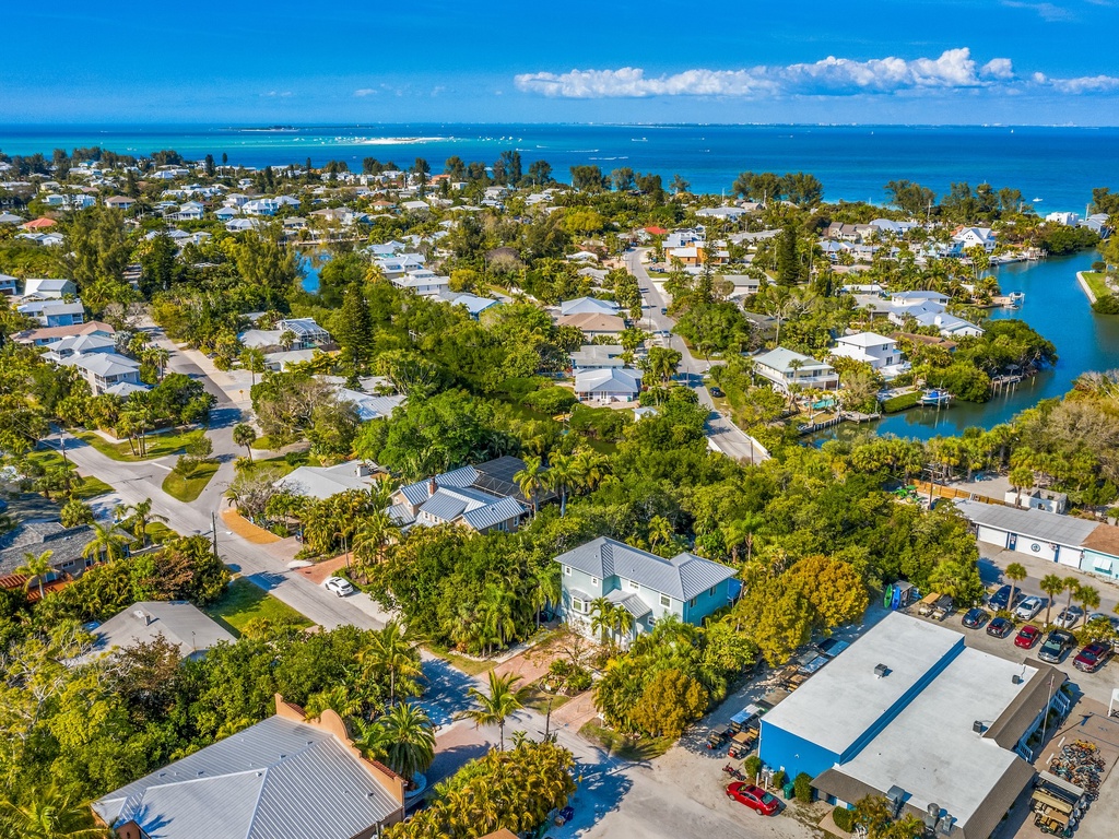 Aerial view of coastal vacation community with tropical homes nestled among lush trees near pristine blue waters.