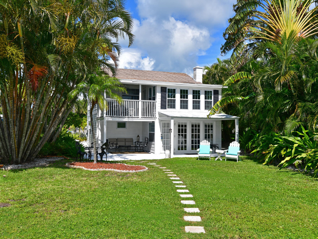 Charming two-story coastal home surrounded by lush tropical landscaping with palm trees and manicured lawn.