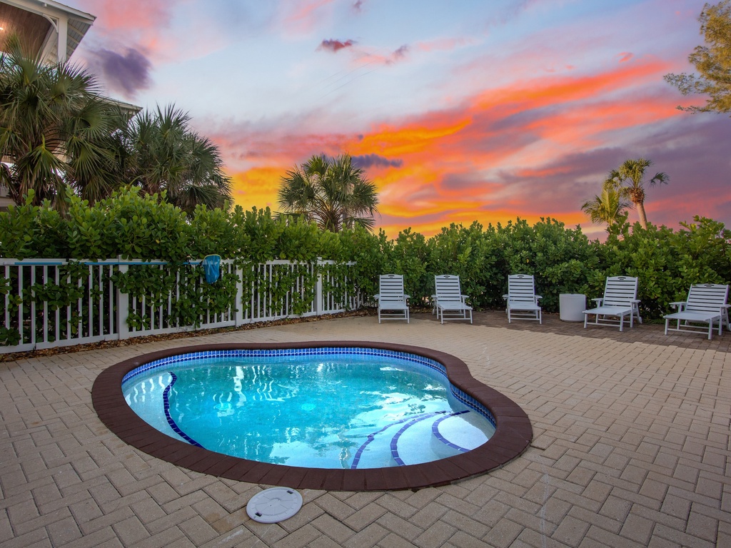 Stunning sunset paints the sky while tropical palms frame this private pool oasis with comfortable lounge chairs.