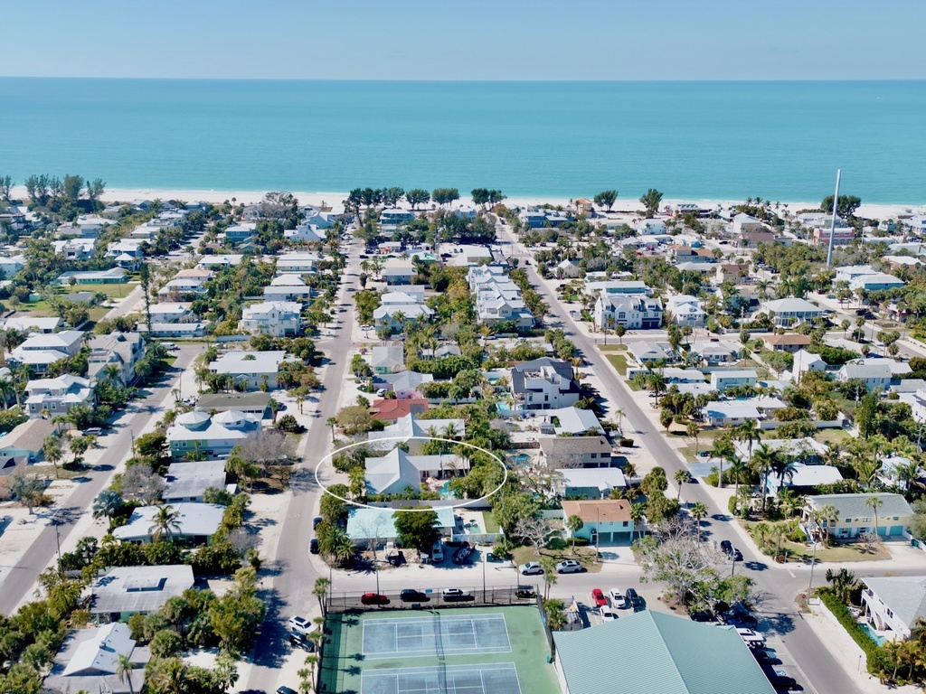 Aerial view of a charming beachside neighborhood with tree-lined streets leading to pristine white sand beaches and turquoise waters.