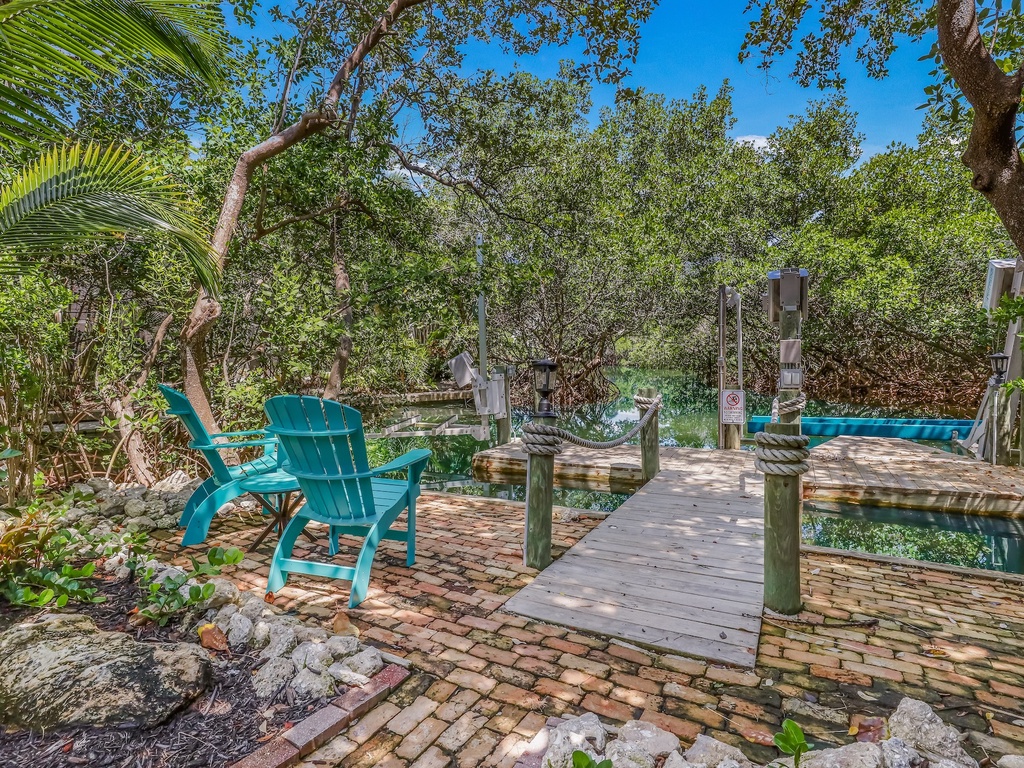 Tropical waterfront dock with turquoise chairs and lush mangrove surroundings creates a peaceful retreat.