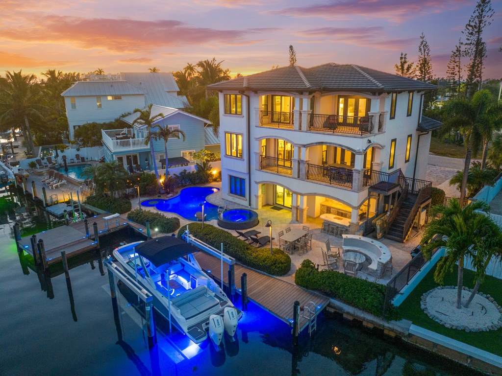 Luxury home featuring private dock, pools, and tropical landscaping with vibrant sunset views.