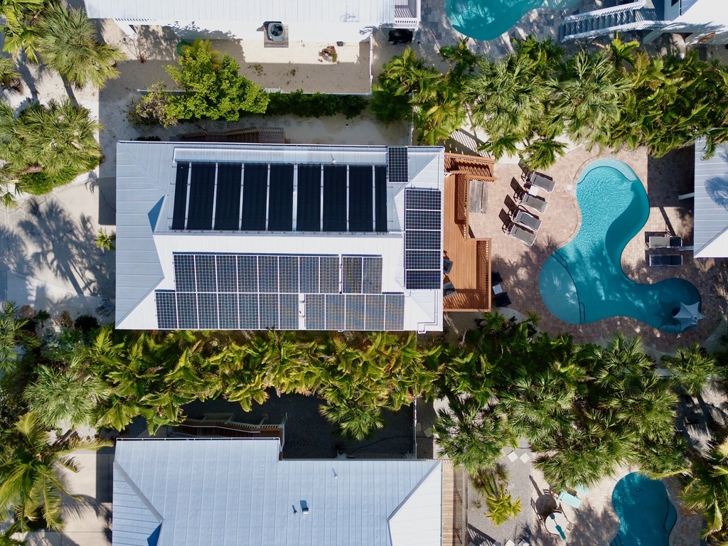 Aerial view of a tropical vacation rental with solar panels, swimming pool, and lush palm trees creating a private paradise.