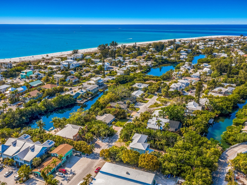 Aerial view showcases a stunning coastal community with winding blue canals threading through lush tropical homes, just steps from pristine white sand beaches.