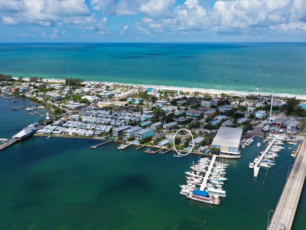 Stunning aerial view of waterfront community featuring marina, beach access, and coastal living surrounded by turquoise waters.