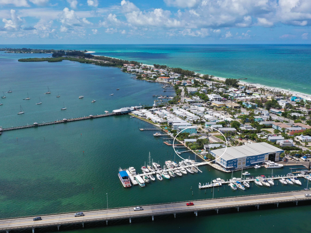 Aerial view of coastal town with marina, beach community, and turquoise waters stretching to the horizon.