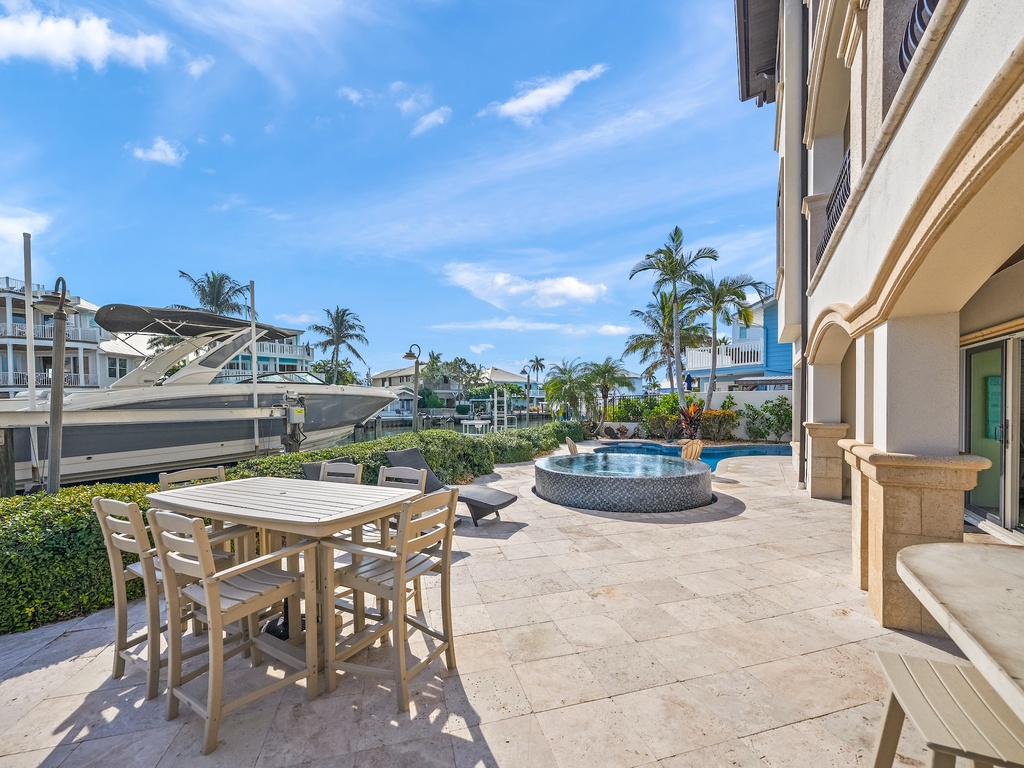 Waterfront patio with outdoor dining and pool, surrounded by tropical palms and marina views.