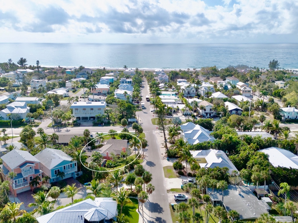 Aerial view of a tropical coastal neighborhood with colorful homes nestled among palm trees, just steps from pristine beaches.