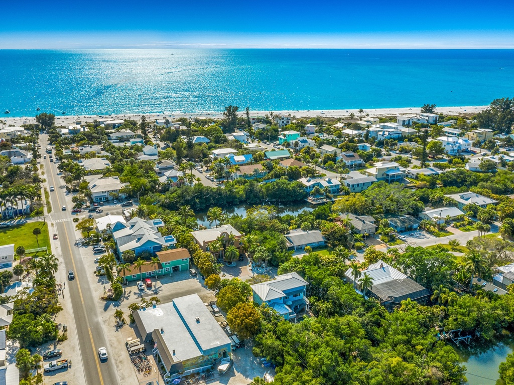 Aerial view of a charming beachside community with tree-lined streets leading to pristine white sand beaches and turquoise waters.