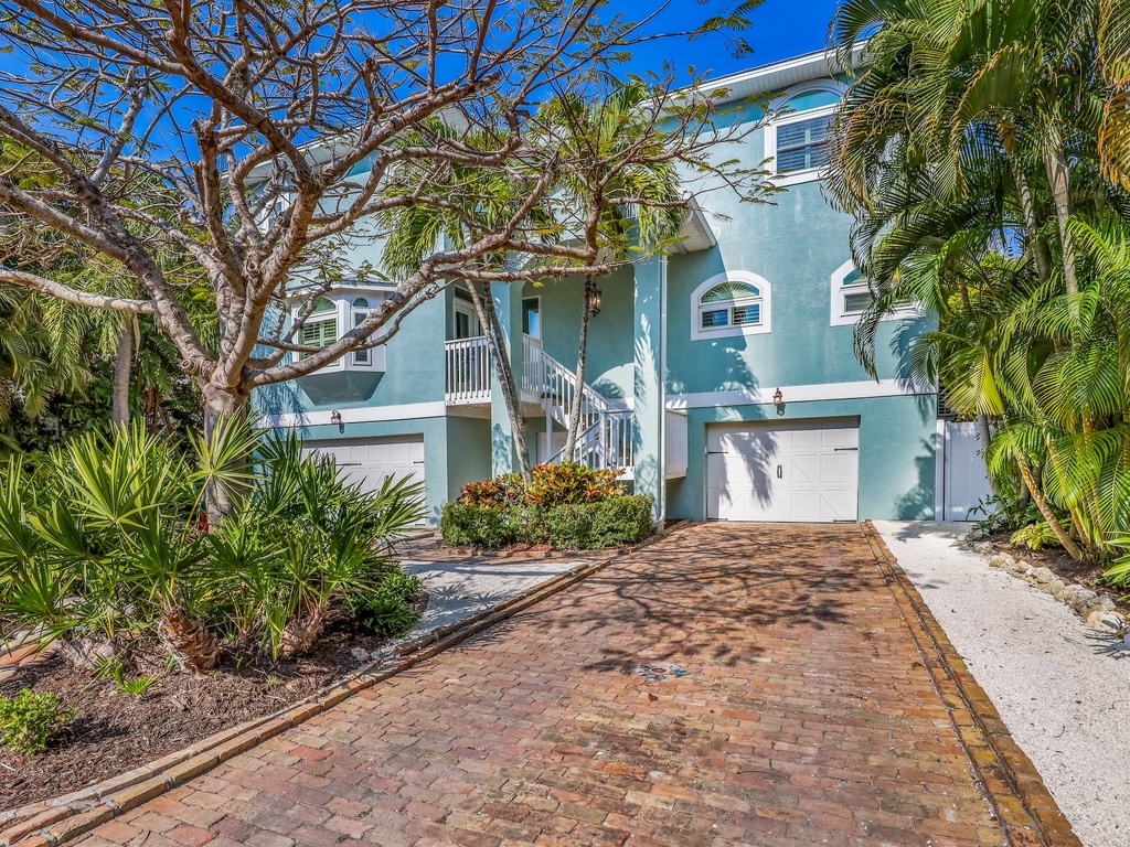 Charming tropical property featuring a distinctive turquoise facade surrounded by lush palm trees and mature landscaping.