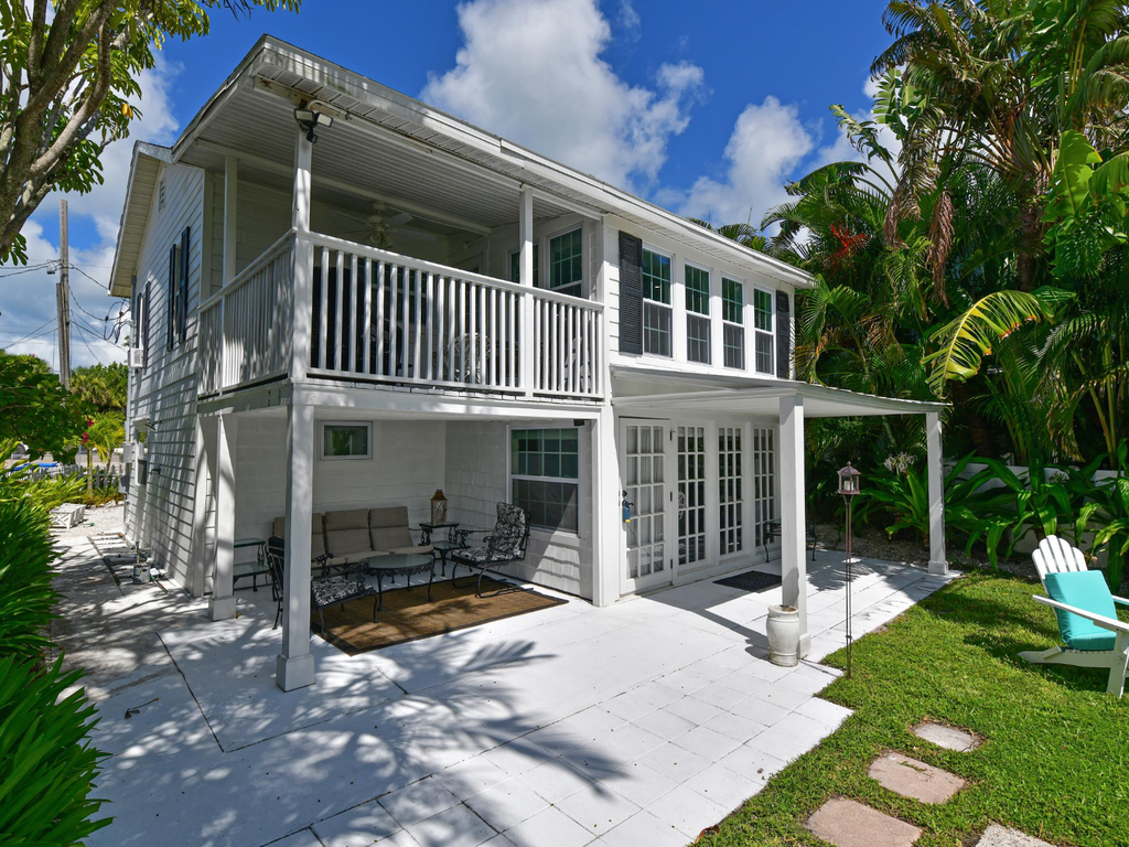 Charming two-story coastal home with covered patio and tropical garden setting surrounded by lush palms and greenery.