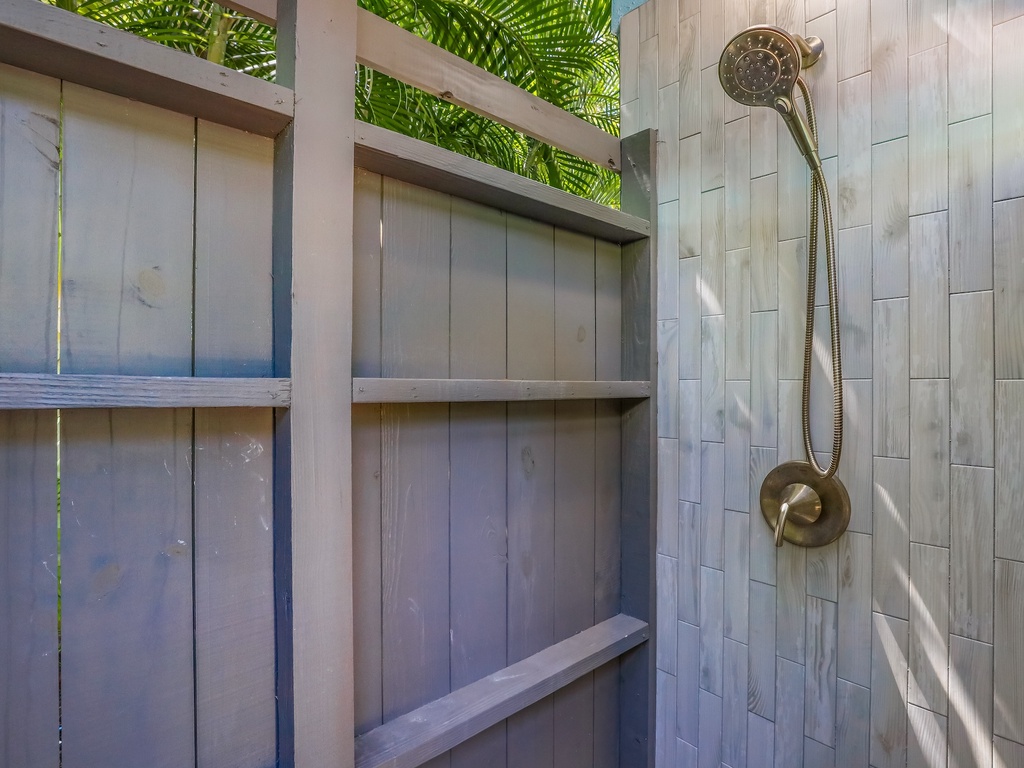 Rinse off in your tropical outdoor shower, where modern brass fixtures meet natural wood under swaying palms.