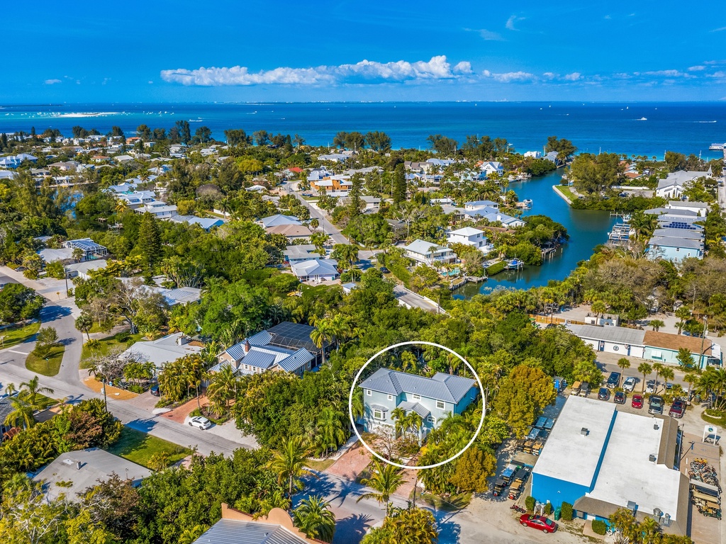 Aerial view of a coastal neighborhood with tropical landscaping, showing the property's location near waterfront amenities and beach access.