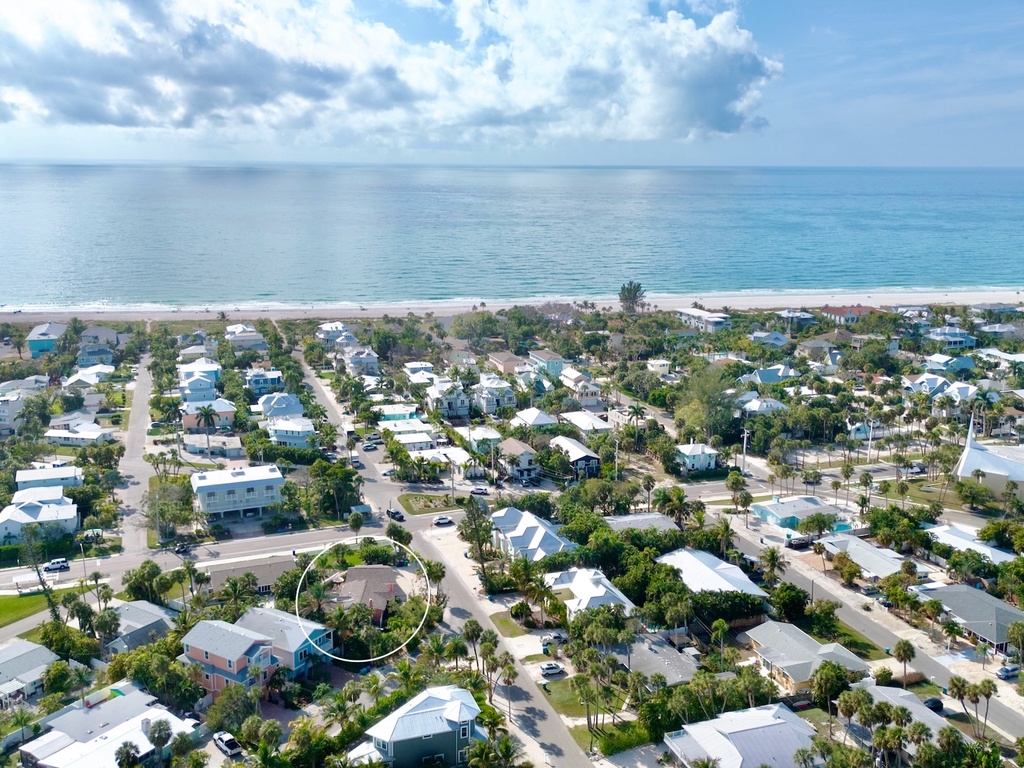 Aerial view of a charming beachfront community with tropical homes nestled between palm trees and pristine coastline.