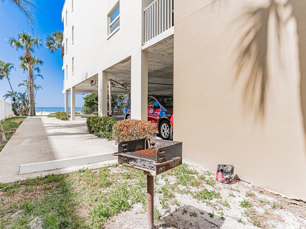 Beachfront property with covered parking, BBQ grill, and tropical landscaping near the sandy shore.