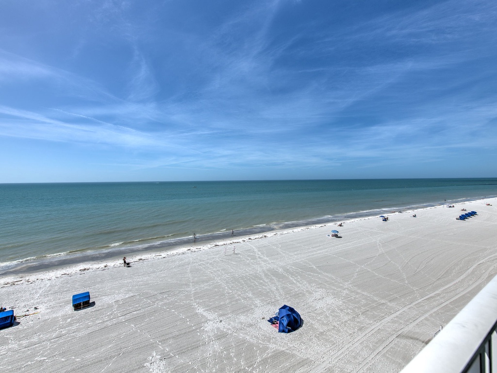 Pristine white sand beach stretches endlessly along emerald waters, visible from the property balcony.