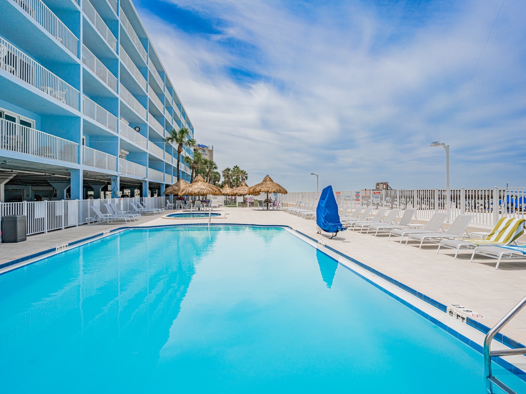 Sparkling pool surrounded by comfortable loungers and tropical tiki huts, creating the perfect beachside retreat atmosphere.