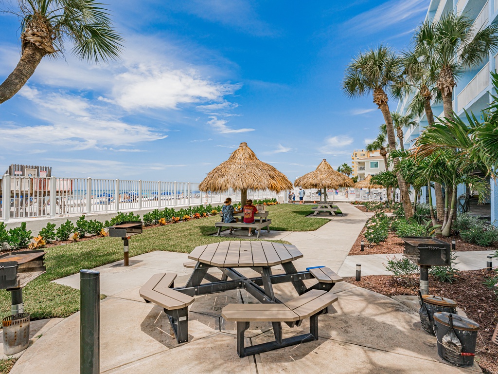 Tropical beachfront property featuring thatched-roof cabanas, picnic tables, and lush palm landscaping with direct beach access.