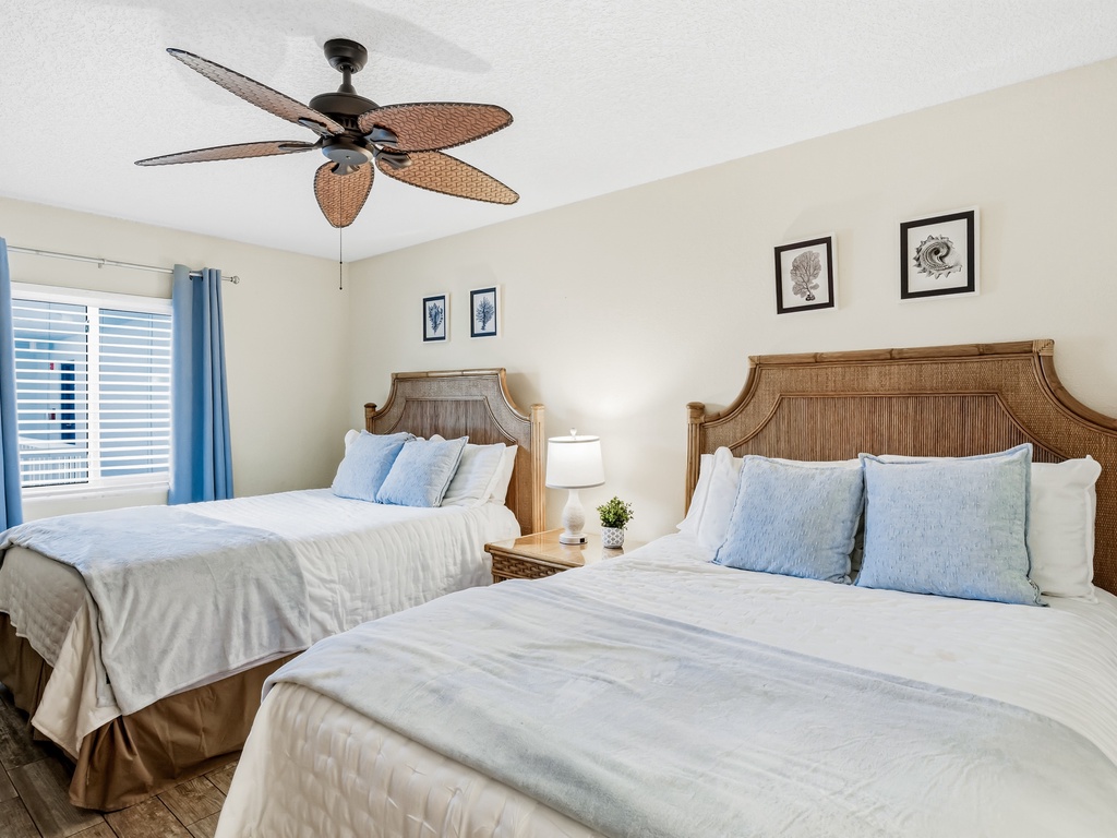 Rest easy in your coastal-themed bedroom with two comfortable beds, tropical ceiling fan, and peaceful blue accents creating the perfect retreat.