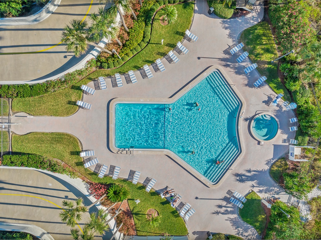 Aerial view of the resort-style pool complex with expansive deck area, spa, and tropical landscaping throughout the property grounds.