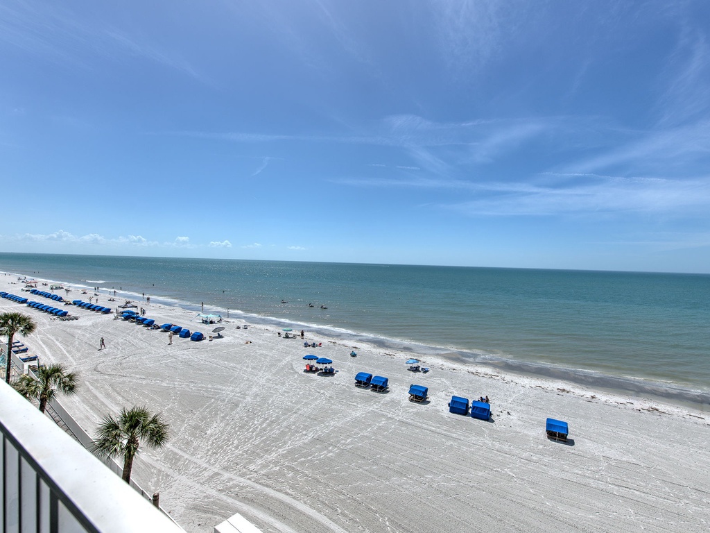 Pristine white sand beach stretches along emerald waters with blue umbrellas and comfortable loungers awaiting guests.