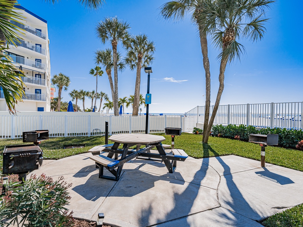 Beachside BBQ area with palm-shaded picnic table and grills - perfect for your tropical dining experience.