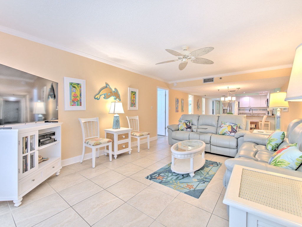 Relax in your bright, coastal-themed living space with comfortable sectional seating, tropical artwork, and modern entertainment center.