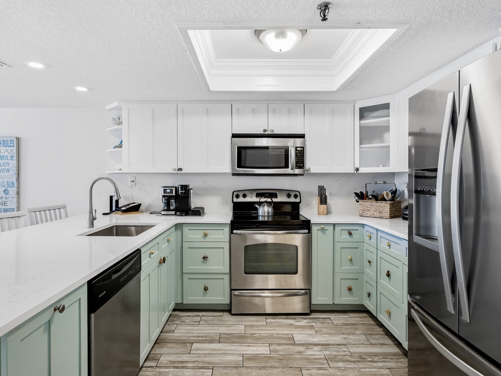 Cook with ease in your fully equipped kitchen featuring stainless appliances, ample counter space, and coastal-inspired mint cabinetry.