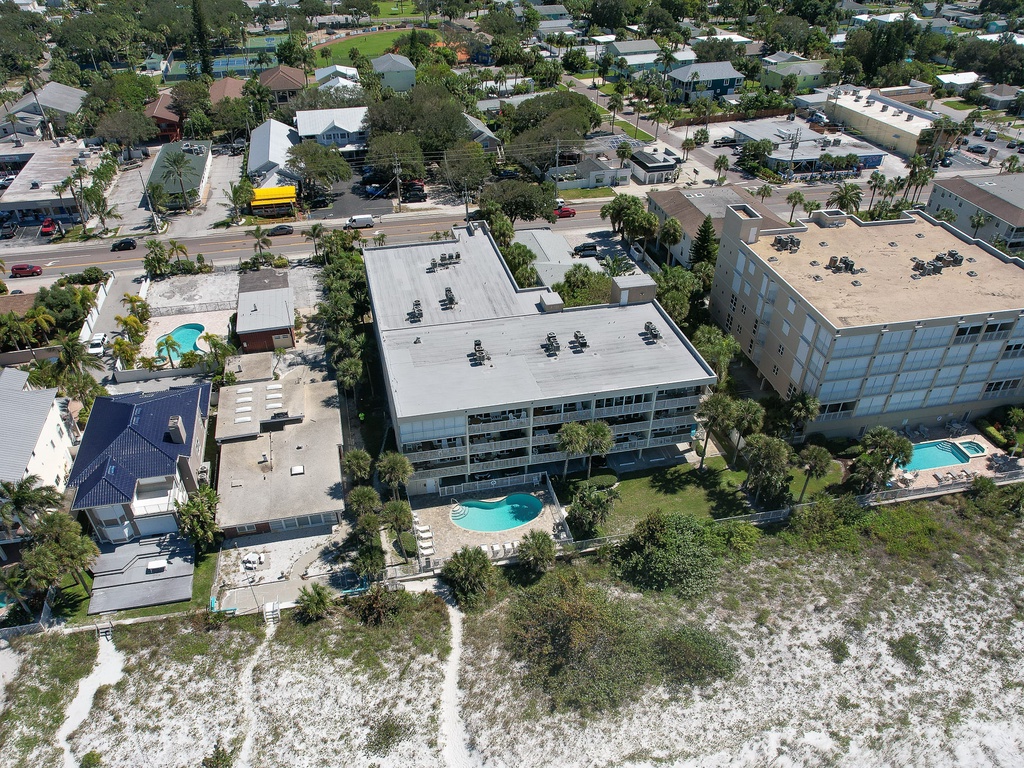 Aerial view of beachfront resort buildings nestled among palm trees, with multiple pools and direct beach access in a tropical coastal setting.