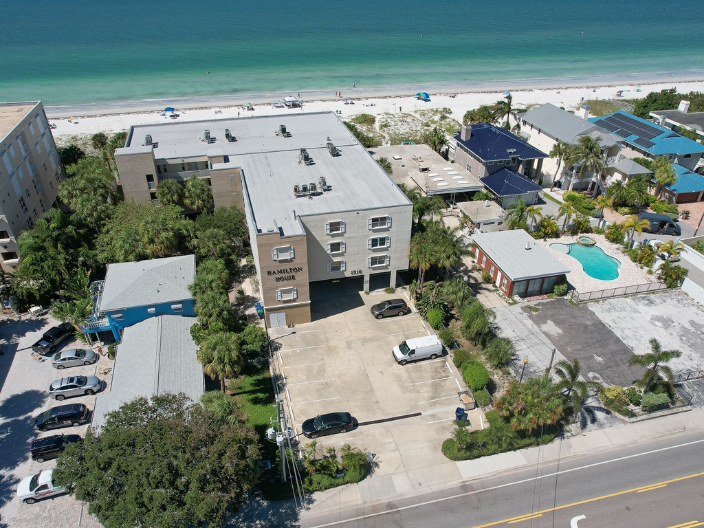 Beachfront property offering stunning aerial perspective of pristine white sand beach and turquoise waters, surrounded by tropical palm trees and neighboring vacation homes.