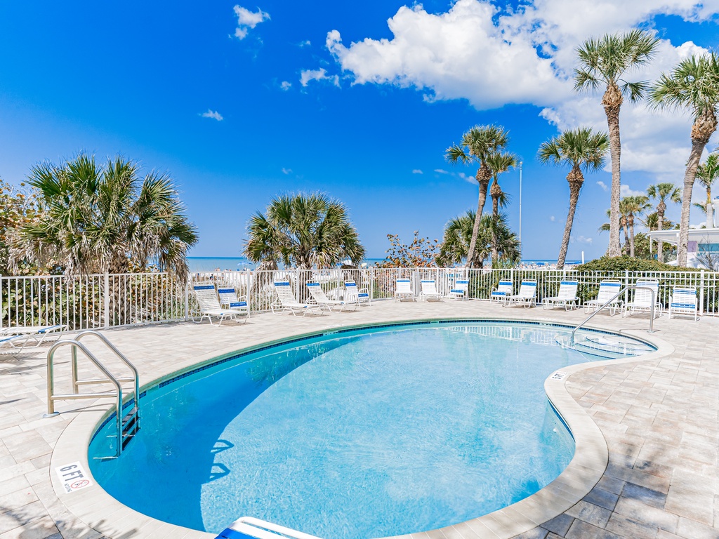 Beachfront pool area featuring crystal-clear water, palm trees, and direct beach access under brilliant blue skies.